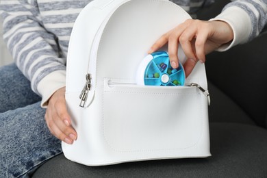 Photo of Woman putting pill box into backpack on sofa, closeup