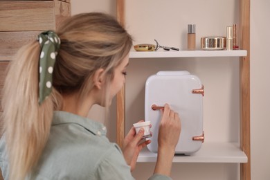 Woman taking cosmetic product from mini fridge indoors, focus on hands