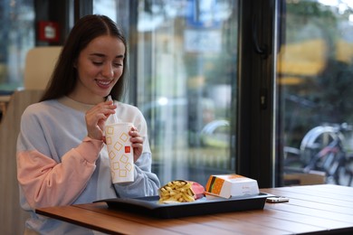 Photo of Lviv, Ukraine - September 26, 2023: Woman with McDonald's drink, burger and french fries at table in restaurant, space for text