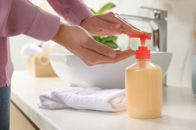 Photo of Woman using liquid soap dispenser in bathroom, closeup