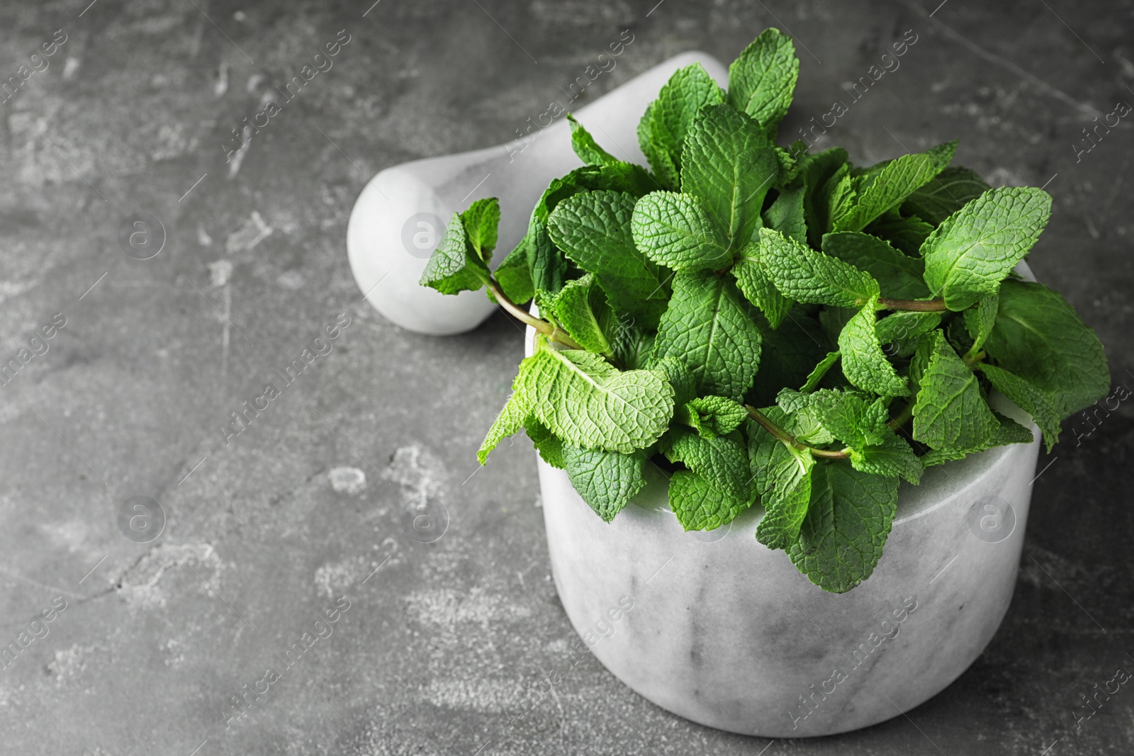 Photo of Marble mortar full of fresh green mint on grey background, space for text