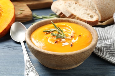 Photo of Delicious pumpkin soup in bowl on blue wooden table