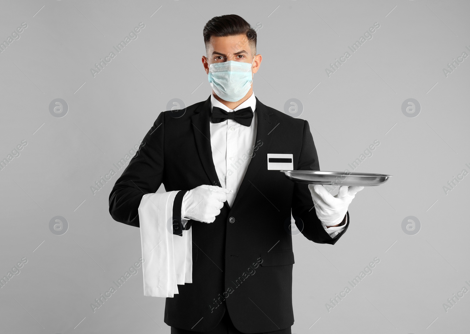 Photo of Waiter in medical face mask with empty tray on light grey background