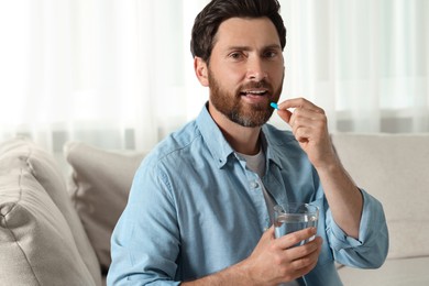 Handsome man with glass of water taking pill at home