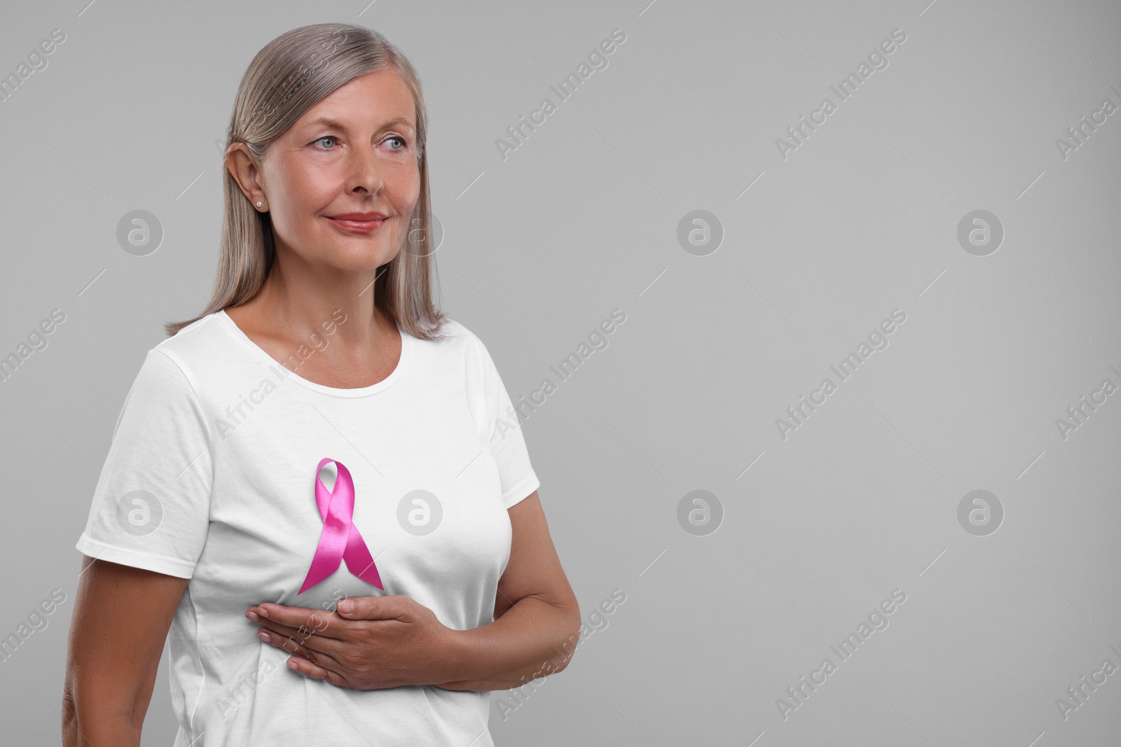 Photo of Beautiful senior woman with pink ribbon on light grey background, space for text. Breast cancer awareness