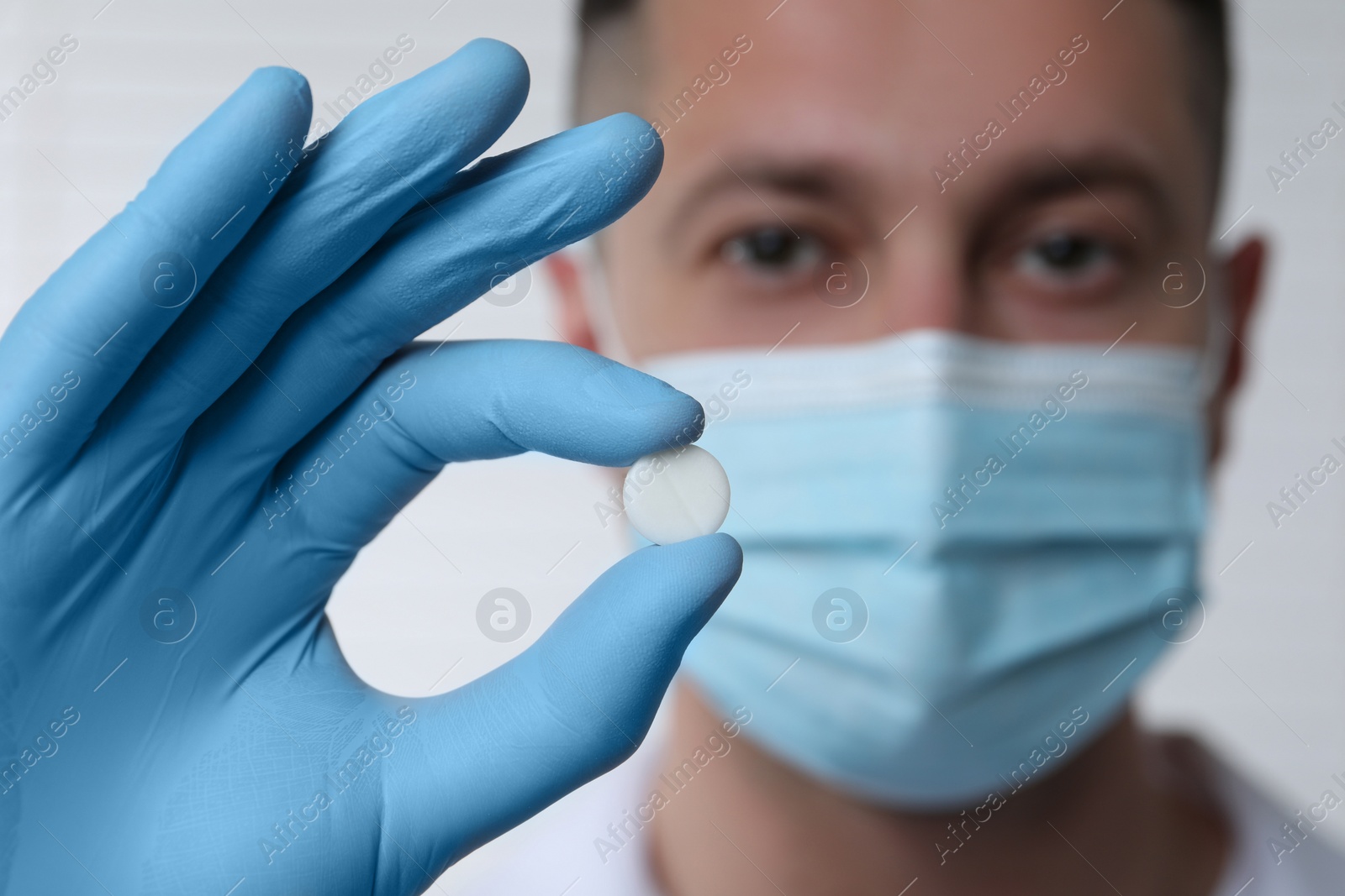 Photo of Doctor holding pill on light background, selective focus. Space for text