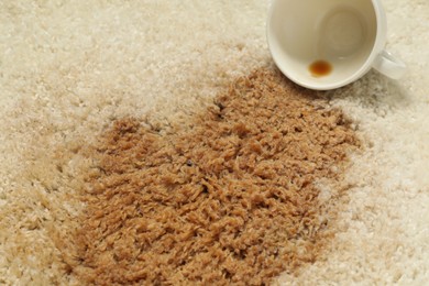 Photo of Overturned cup and spilled coffee on beige carpet, closeup
