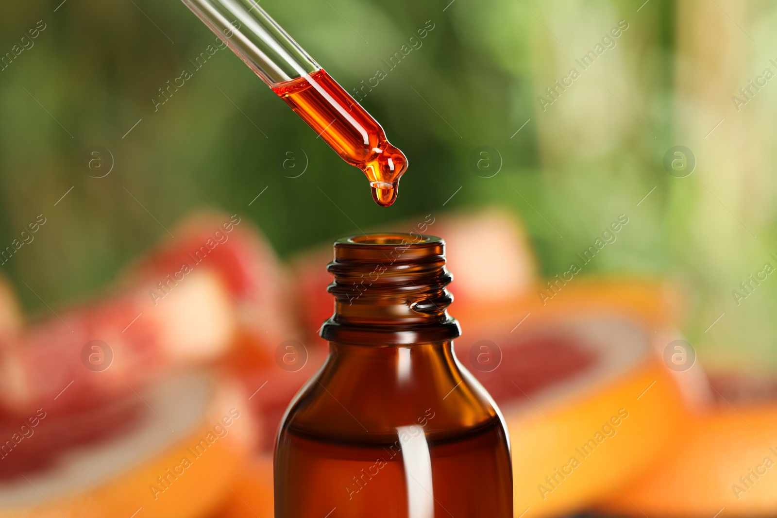 Photo of Dripping citrus essential oil from pipette into bottle on blurred background, closeup