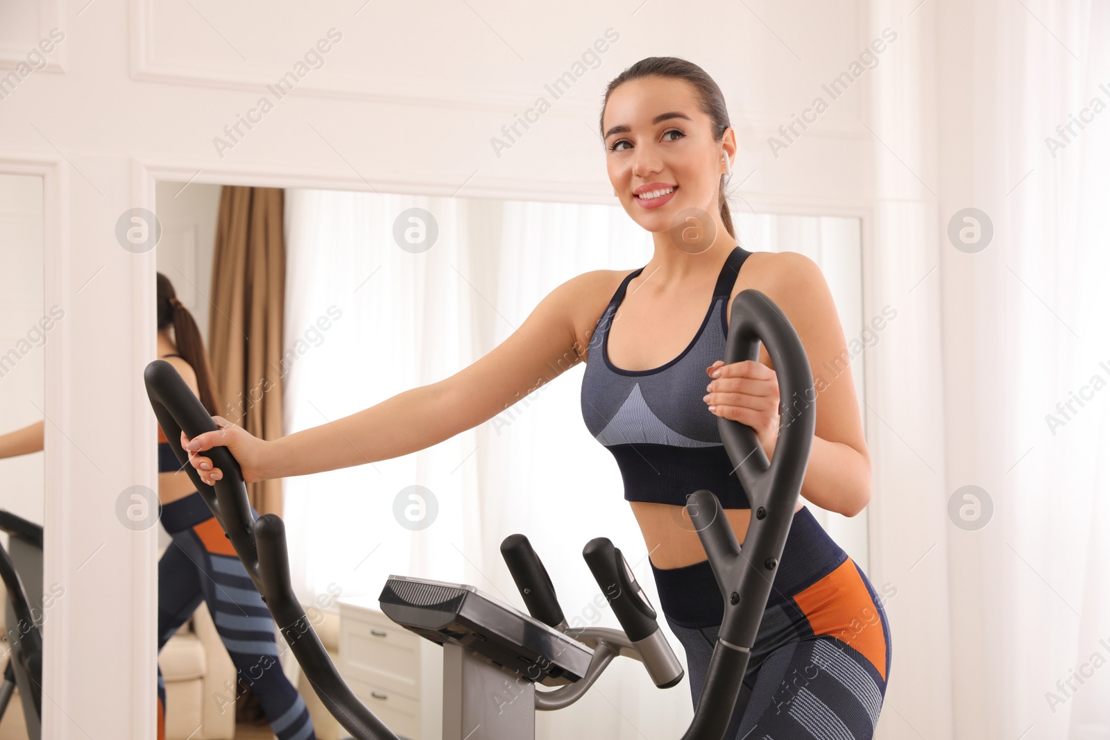 Photo of Woman using modern elliptical machine at home