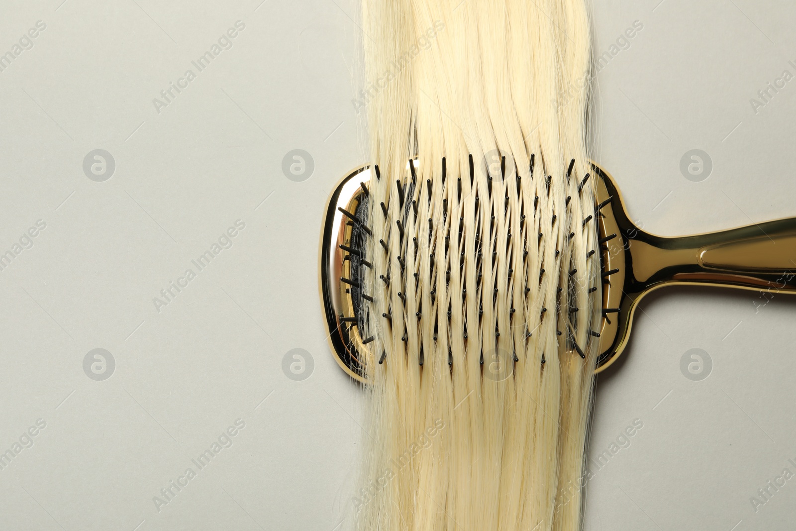Photo of Stylish brush with blonde hair strand on light grey background, top view. Space for text