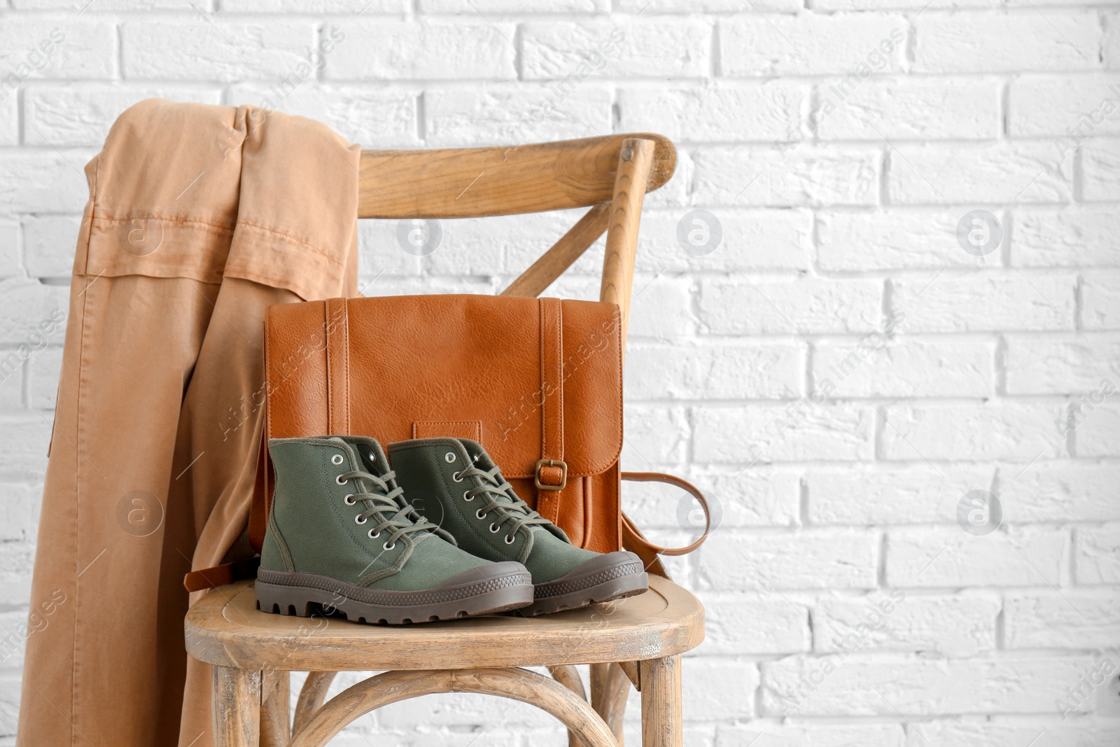 Photo of Comfortable casual female shoes and bag on chair against white brick wall