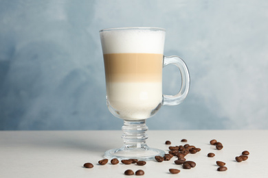 Photo of Delicious latte macchiato and coffee beans on white table against light blue background