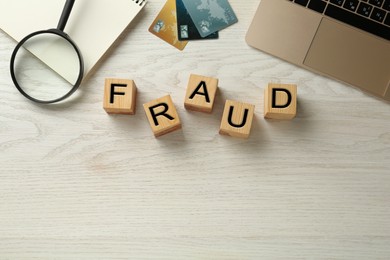Photo of Wooden cubes with word Fraud, credit cards, laptop and magnifying glass on white table, flat lay. Space for text