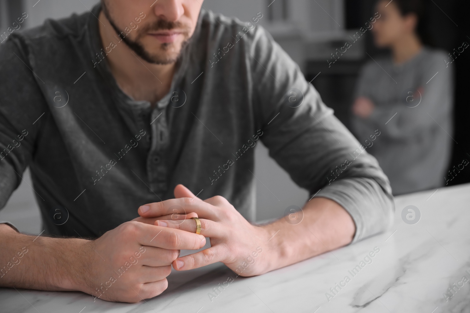 Photo of Man taking off wedding ring at white marble table indoors, closeup. Couple on verge of divorce