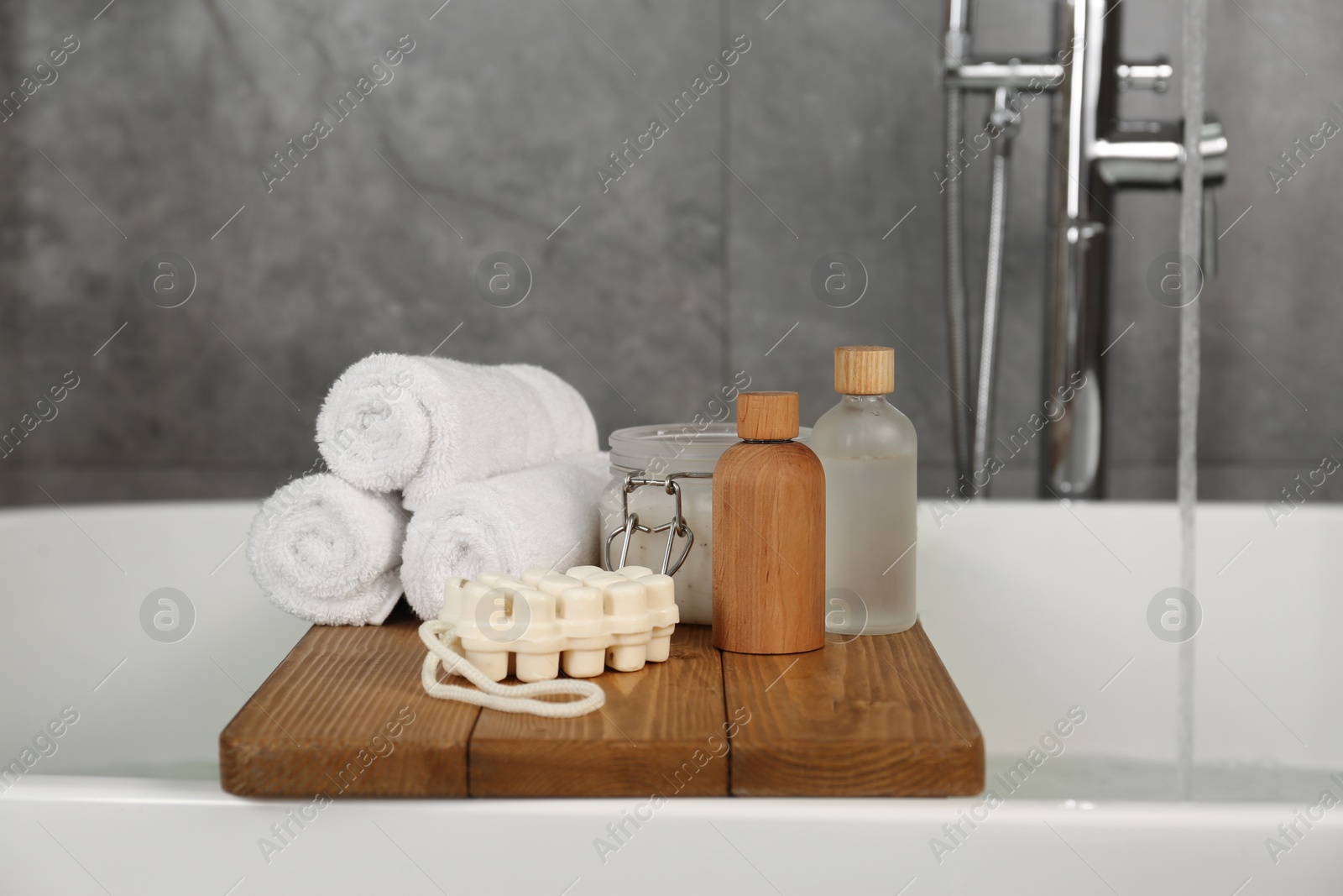 Photo of Wooden tray with spa products and towels on bath tub in bathroom