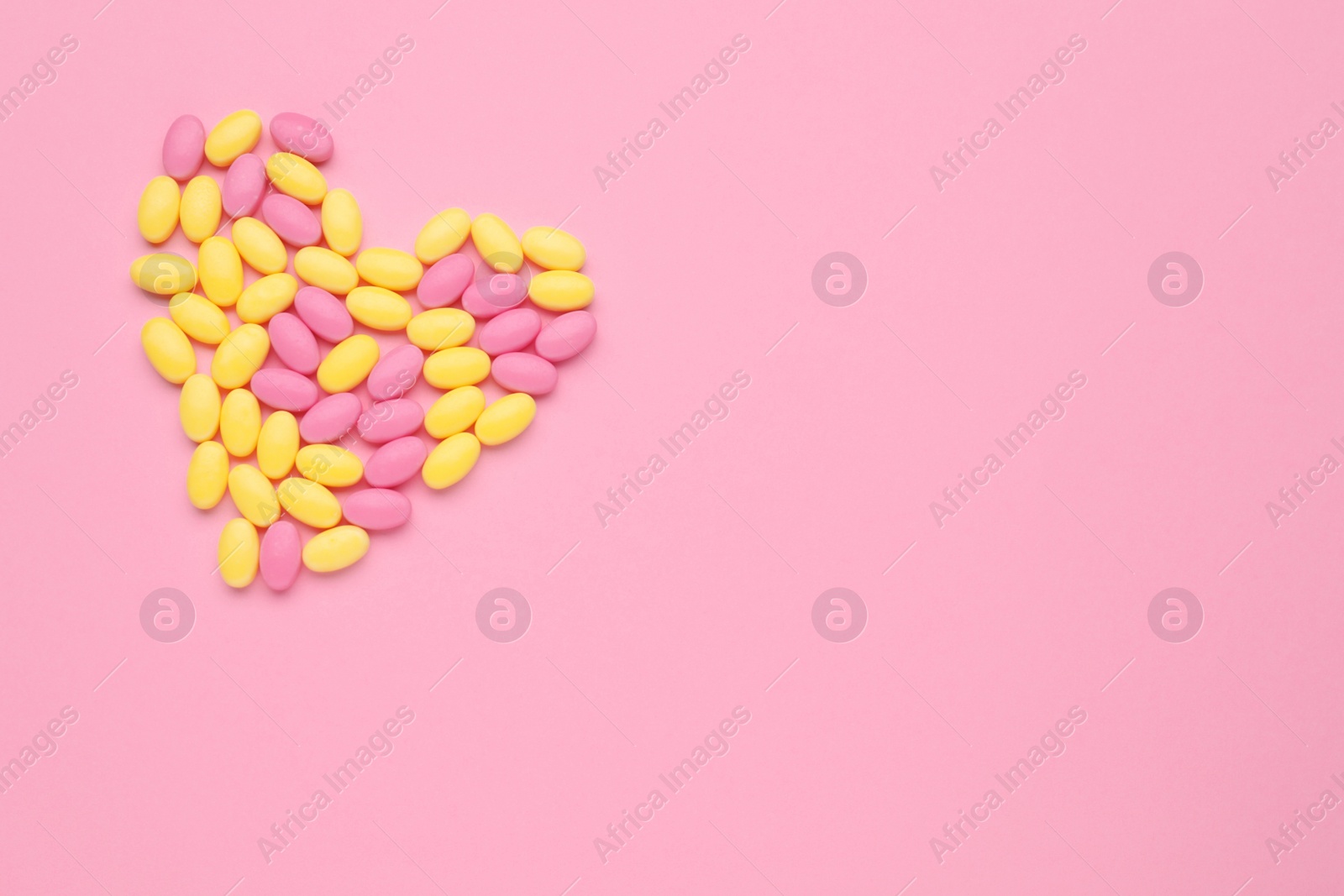 Photo of Heart made of bright dragee candies on pink background, flat lay. Space for text