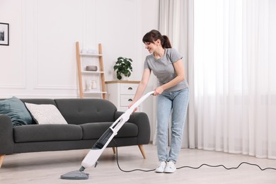 Photo of Happy young housewife cleaning floor with steam mop at home