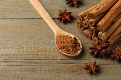 Photo of Spoon with cinnamon powder, sticks and star anise on wooden table. Space for text
