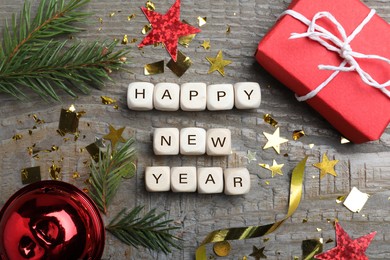 Photo of Phrase Happy New Year made of cubes and festive decor on wooden background, flat lay