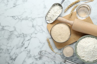 Leaven, flour, ears of wheat, rolling pin, whisk and water on white marble table, flat lay. Space for text