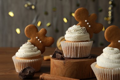 Tasty Christmas cupcakes with gingerbread man cookies on wooden table