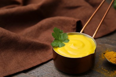 Photo of Saucepan with tasty curry sauce, powder and parsley on wooden table, closeup