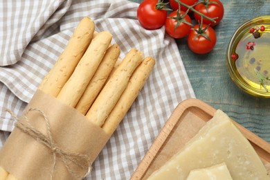 Tasty grissini, tomatoes, oil and cheese on light blue wooden table, flat lay