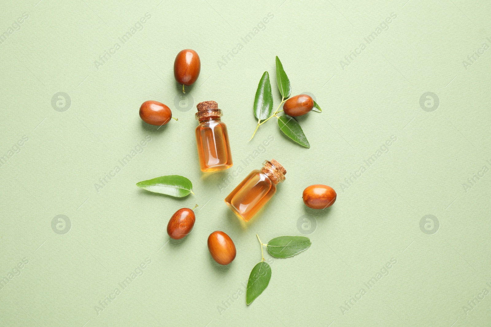 Photo of Glass bottles with jojoba oil and seeds on green background, flat lay
