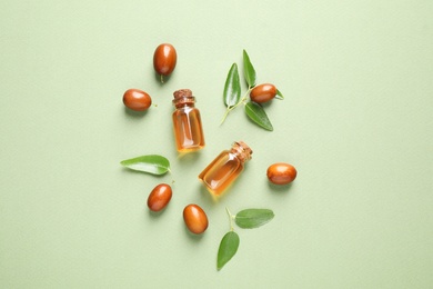 Glass bottles with jojoba oil and seeds on green background, flat lay