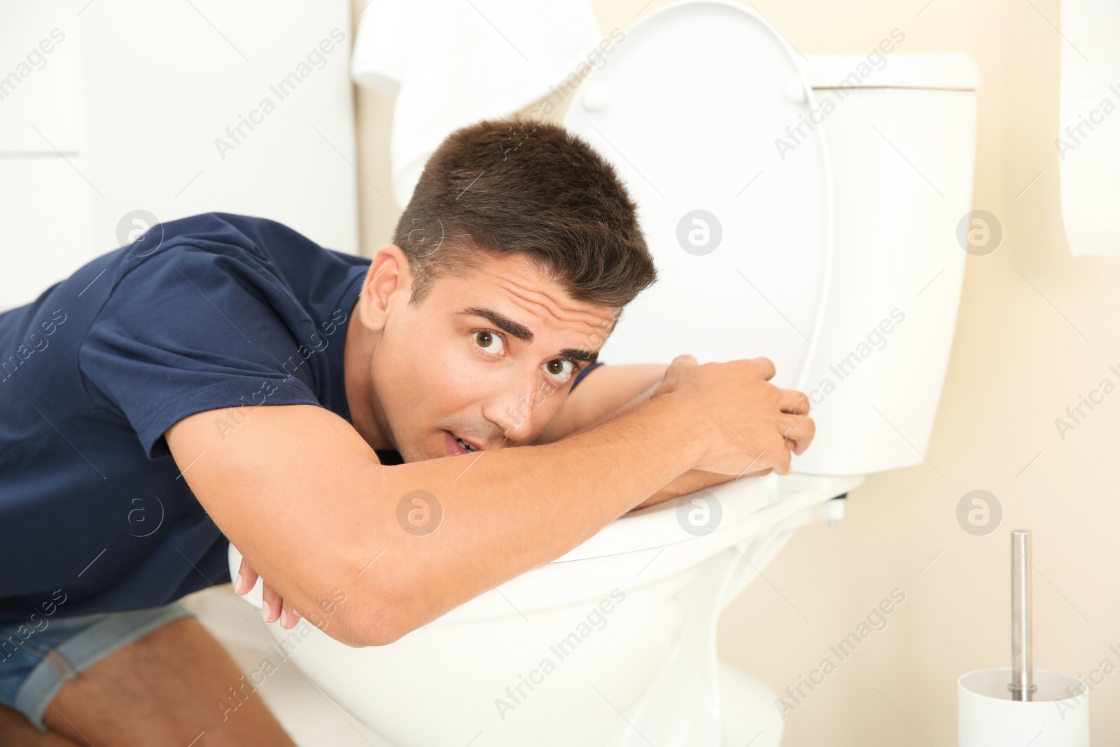 Photo of Young man vomiting in toilet bowl at home