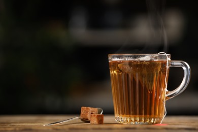 Photo of Tea bag in glass cup of hot water and sugar on wooden table against blurred background