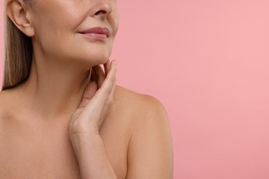 Photo of Mature woman touching her neck on pink background, closeup. Space for text