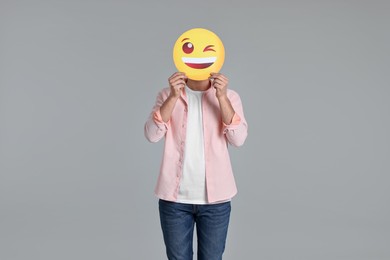 Photo of Man covering face with happy winking emoticon on grey background