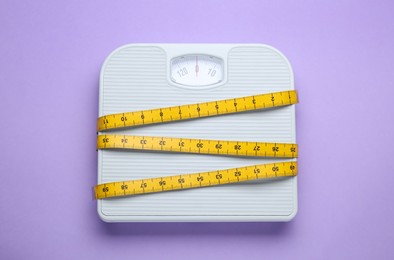 Scales and measuring tape on violet background, top view