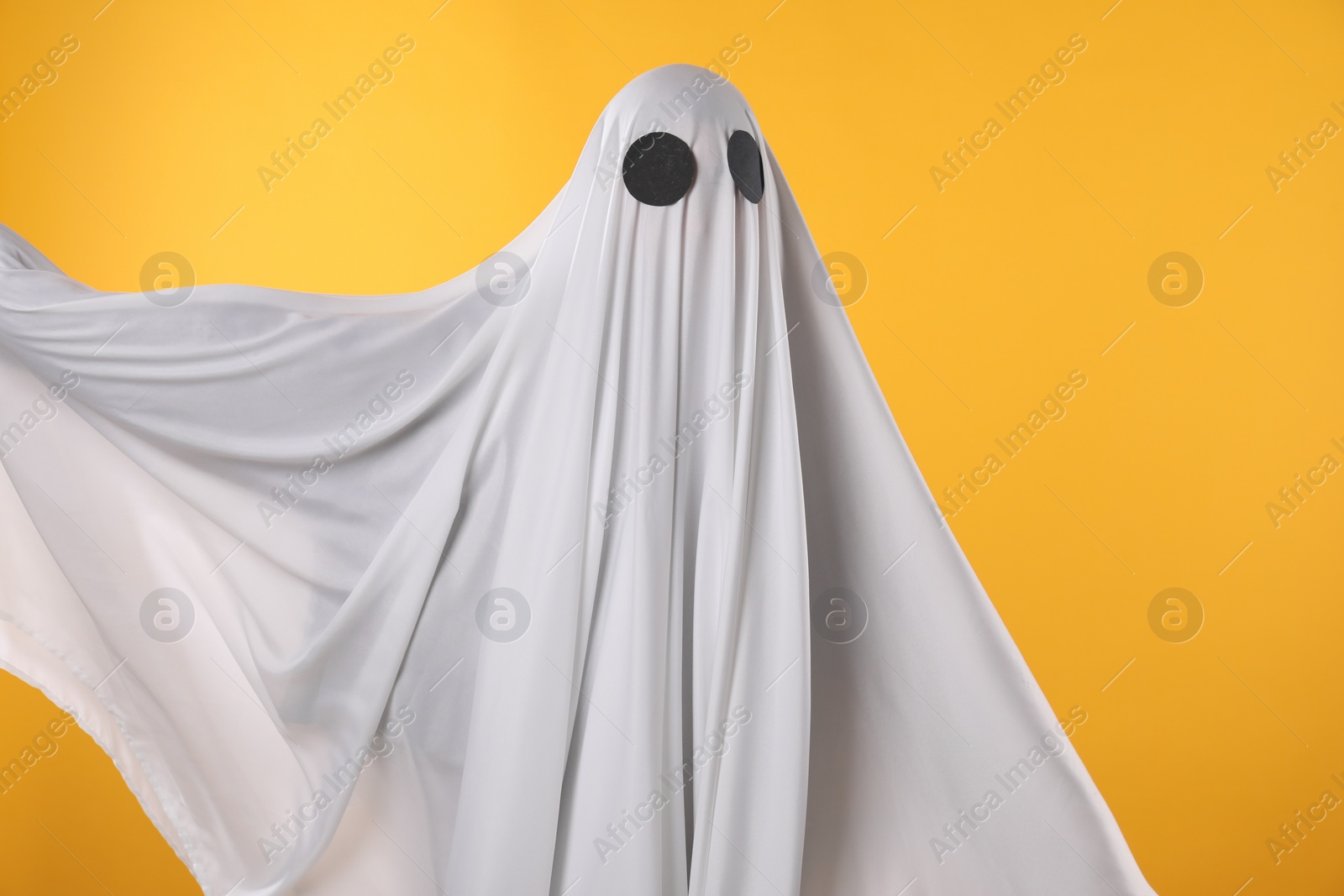 Photo of Creepy ghost. Person covered with white sheet on yellow background