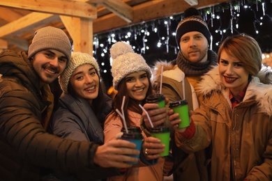 Happy friends with cups of mulled wine at winter fair