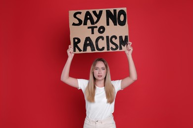 Young woman holding sign with phrase Say No To Racism on red background