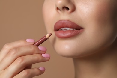 Photo of Young woman applying beautiful nude lip pencil on beige background, closeup