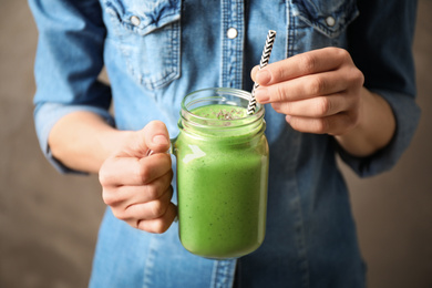 Photo of Woman holding tasty kale smoothie on brown background, closeup