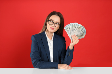 Young woman with money at table on crimson background