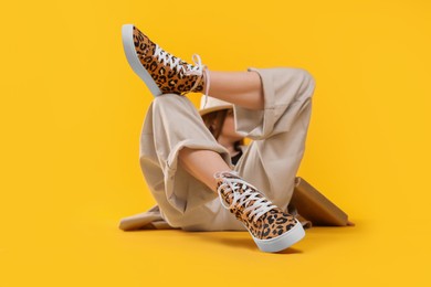 Photo of Stylish woman posing in classic old school sneakers with leopard print on orange background, selective focus