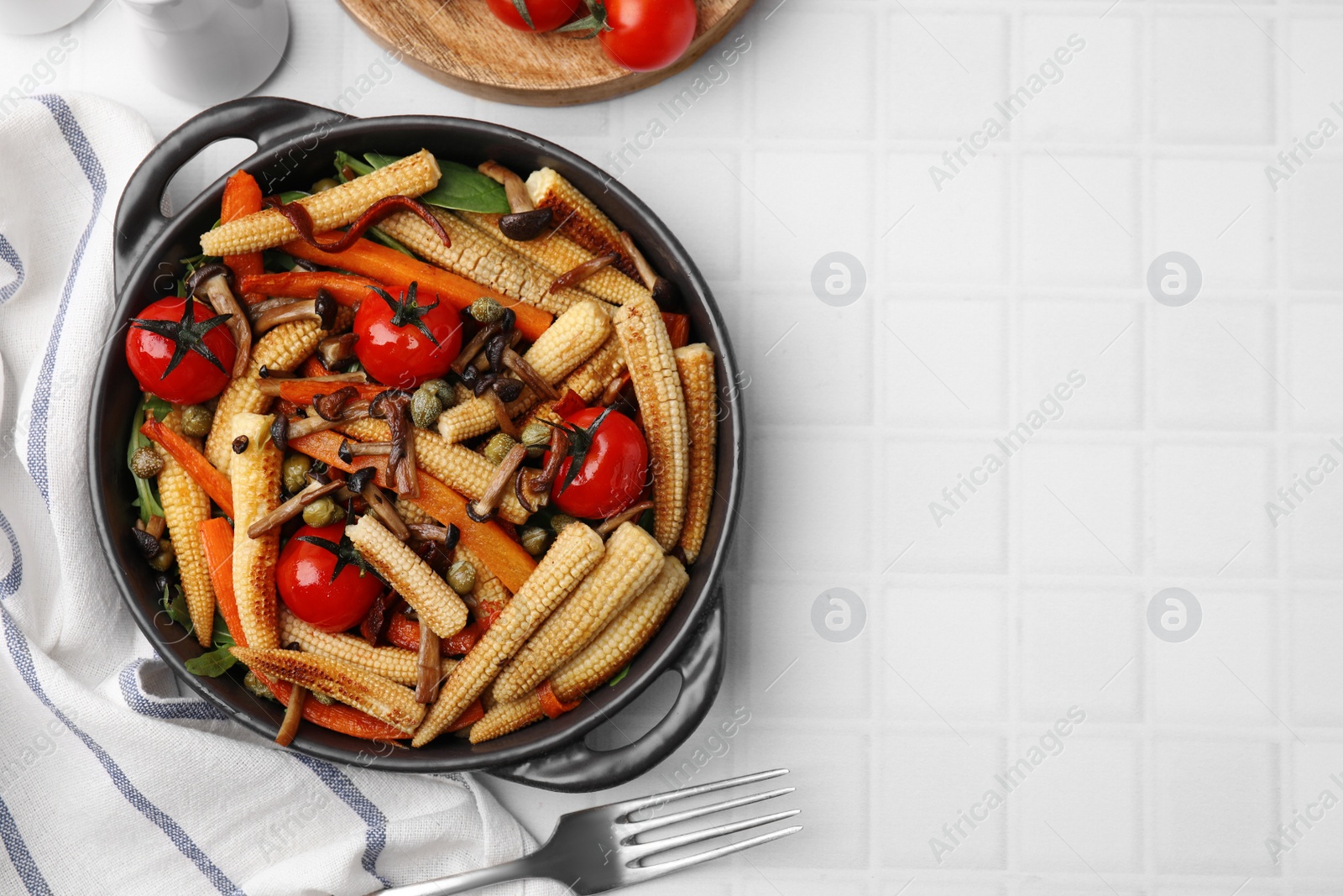 Photo of Tasty roasted baby corn with tomatoes, capers and mushrooms on white tiled table, flat lay. Space for text