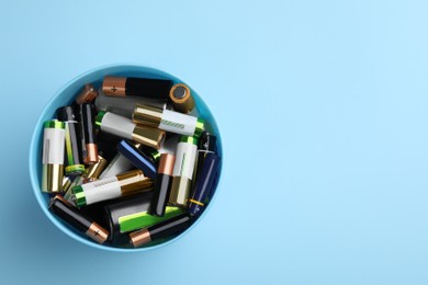 Used batteries in bucket on light blue background, top view. Space for text