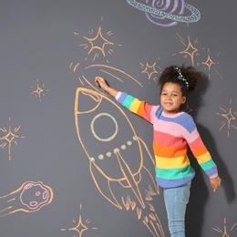 African-American child playing with chalk rocket drawing on grey background