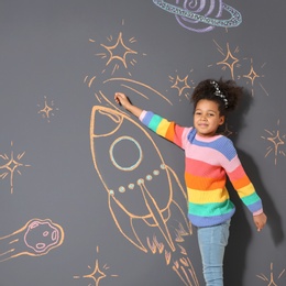 Photo of African-American child playing with chalk rocket drawing on grey background