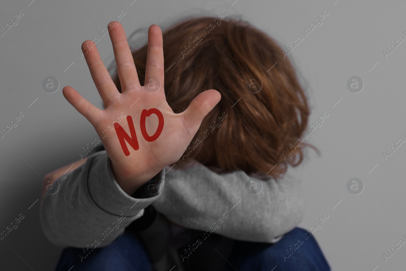 Image of Child abuse. Boy making stop gesture near grey wall, selective focus. No written on his hand