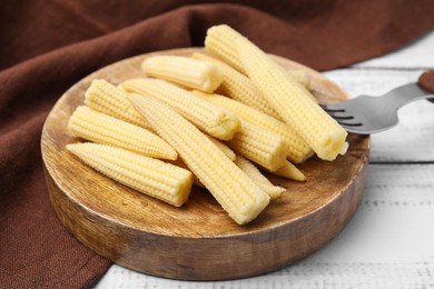 Photo of Pickled baby corn and fork on white wooden table, closeup