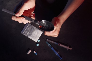 Woman preparing drug with spoon and lighter above table, closeup