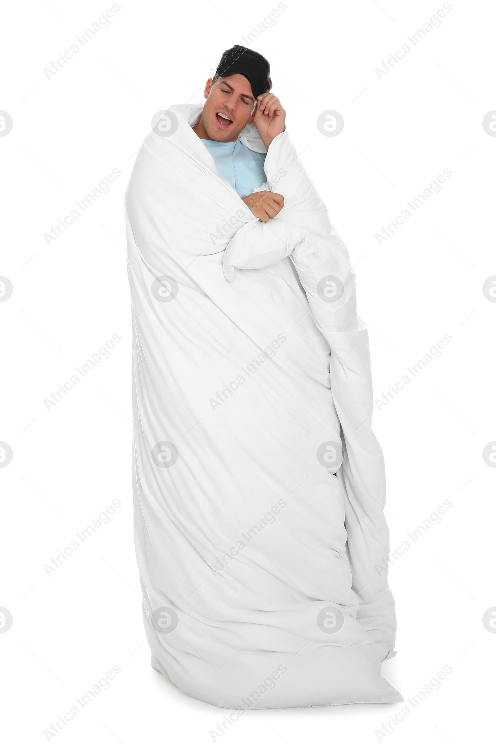 Photo of Man in sleeping mask wrapped with blanket yawning on white background