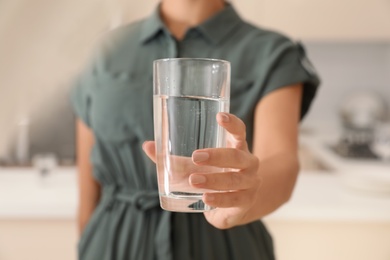 Photo of Woman holding glass with pure water in kitchen, closeup